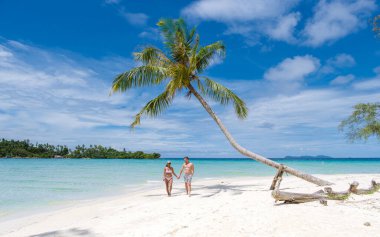 Taylandlı kadınlar ve beyaz erkekler Koh Kood Tayland adasında tropik bir plajda yürüyorlar.