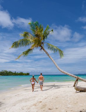 Koh Kood Tayland adasında palmiye ağaçları olan tropik bir sahil. Beyaz tropikal sahilde palmiye ağaçları sallanıyor. Mavi okyanusta birkaç erkek ve kadın Tayland 'da tatilde.