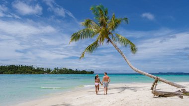 Koh Kood Tayland adasında palmiye ağaçları olan tropik bir sahil. Beyaz tropikal sahilde palmiye ağaçları sallanıyor. Mavi okyanusta birkaç erkek ve kadın Tayland 'da tatilde.