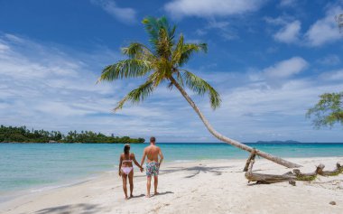 Tayland 'da palmiye ağaçlarıyla tropik bir sahilde yürüyen erkek ve kadınlar.