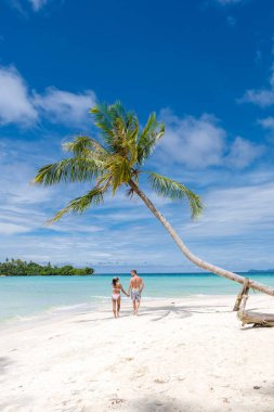 Tayland 'da palmiye ağaçlarıyla tropik bir sahilde yürüyen erkek ve kadınlar.
