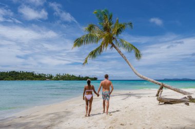 Koh Kood Tayland adasında tropik bir plajda palmiye ağaçları olan Asyalı kadınlar ve beyaz erkekler. Mavi okyanuslu beyaz tropikal sahilde asılı palmiye ağaçları 