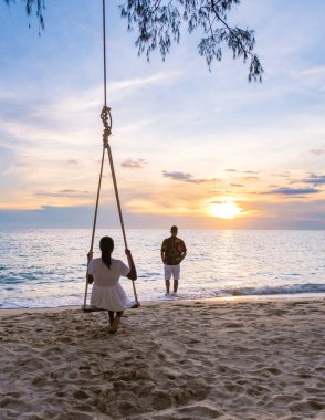 Koh Kood Tayland, plaj salıncaklı tropik bir sahil cenneti. Birkaç erkek ve kadın, güzel bir tropikal kumsal yaz tatilinde hindistan cevizi palmiyesinin altında salıncakta sallanıyor.