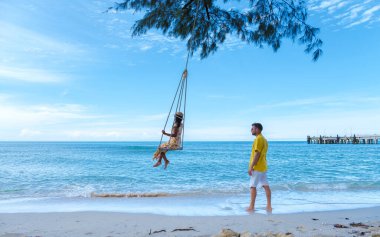 Tropik Koh Kood Adası veya Koh Kut Tayland. Orta yaşlı bir çift kumsalda salıncakla eğleniyor.