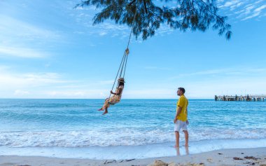 Bir çift Asyalı Taylandlı kadın ve Avrupalı erkek salıncaklı bir plajda, Koh Kood veya Koh Kut Tayland. 