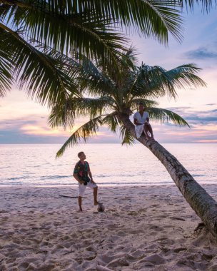 Koh Kood ya da Koh Kut Tayland 'daki plajda asılı duran palmiye ağacından gün batımını izleyen bir çift kadın ve erkek.. 