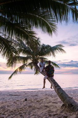 Koh Kood ya da Koh Kut Tayland 'daki plajda asılı duran palmiye ağacından gün batımını izleyen bir çift kadın ve erkek.. 