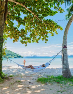 Erkekler ve kadınlar tropik bir plajda dinleniyorlar. Koh Mak tropik adası Tayland 'ın palmiye ağaçları arasındaki sahilde hamak..