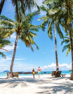Koh Kham Trat Thailand, couple men and women walking on a white tropical beach with palm trees in swimming clothes clipart