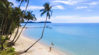 Bir çift Asyalı Taylandlı kadın ve Avrupalı erkek salıncaklı bir plajda, Koh Kood veya Koh Kut Tayland.