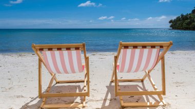 Koh Kood Tayland tropik adasında sandalye ve mavi gökyüzü ile plaj tatili kavramı. Beyaz plajda ve mavi okyanusta renkli kırmızı ve beyaz plaj sandalyesi