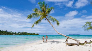 Koh Kood Tayland adasında tatilde olan iki erkek ve kadın. Beyaz tropikal sahilde palmiye ağaçları sallanıyor. Mavi okyanusta birkaç erkek ve kadın Tayland 'da tatilde.