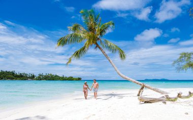 Taylandlı kadınlar ve beyaz erkekler Koh Kood Tayland adasında tropik bir plajda yürüyorlar.