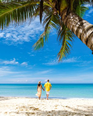 Tropikal Ada Koh Kood veya Koh Kut Tayland Erkek ve kadınları beyaz bir sahilde palmiye ağacının altında yürüyorlar.