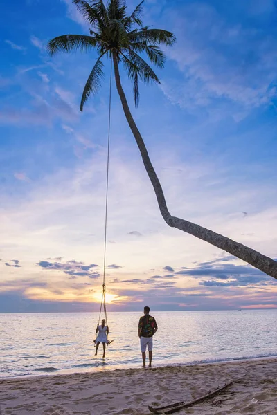 Kumsalda gün batımında salıncakta sallanan çift, Taylandlı kadınlar ve beyaz erkekler günbatımını, Tropikal Ada Koh Kood veya Koh Kut Tayland 'ı izliyor..