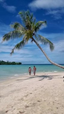 Tropikal Ada Koh Kood veya Koh Kut Tayland Erkek ve kadınları beyaz bir sahilde palmiye ağacının altında yürüyorlar.