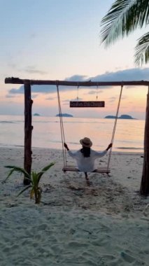 Tropikal ada Koh Chang plaj salıncaklı tropik bir plaj cenneti. Kadınlar, güzel bir tropik plajda hindistan cevizi palmiyesinin altında salıncakta sallanır. Yaz tatili beyazdır.