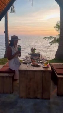 Gün batımında Tayland yemeğiyle sahilde romantik bir akşam yemeği, gün batımında Asyalı Taylandlı kadınlar Koh Mak Tayland adasında akşam yemeği.