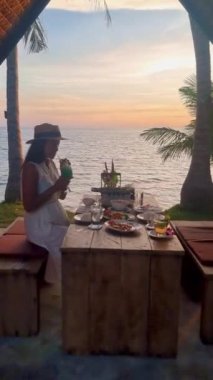Gün batımında Tayland yemekleriyle kumsalda romantik bir akşam yemeği, gün batımında Asyalı Taylandlı kadınlar akşamları Koh Mak Tayland adasında akşam yemeği.