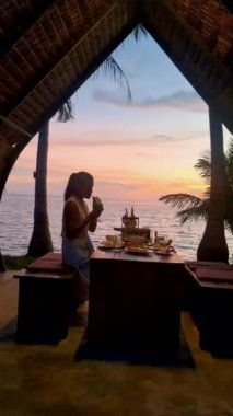Gün batımında Tayland yemeğiyle sahilde romantik bir akşam yemeği, gün batımında Asyalı Taylandlı kadınlar Koh Mak Tayland adasında akşam yemeği.