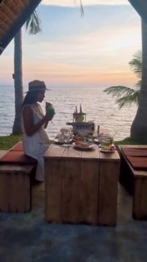 Taylandlı kadınlar gün batımında Tayland yemekleriyle sahilde romantik bir akşam yemeği yiyorlar. Gün batımında Asyalı Taylandlı kadınlar Koh Mak Tayland adasında yemek yiyorlar.