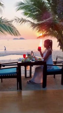 Gün batımında Tayland yemeğiyle sahilde romantik bir akşam yemeği, gün batımında Asyalı Taylandlı kadınlar Koh Chang Tayland sahilinde akşam yemeği.