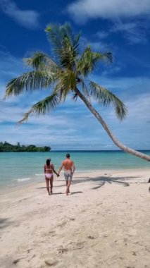 Koh Kood Tayland adasında tatil yapan birkaç beyaz erkek ve Taylandlı kadın. Mavi okyanus ve turkuaz suyla beyaz tropikal sahilde asılı palmiye ağaçları. 