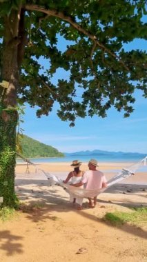 Tayland Koh Mak tropik adasında tropik bir plajda hamakta iki erkek ve kadın.