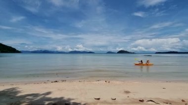 Orta yaşlı bir çift Koh Mak Tayland 'ın tropikal adasının okyanusunda kanoda kürek çekiyorlar. Erkekler ve kadınlar mavi bir okyanusta kano ve palmiye ağaçlı beyaz plajda