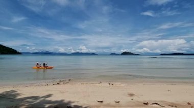 Erkekler ve kadınlar Koh Mak Tayland 'ın tropik adasının okyanusunda bir kanoda kürek çekiyorlar. Erkekler ve kadınlar mavi bir okyanusta kano ve palmiye ağaçlı beyaz plajda