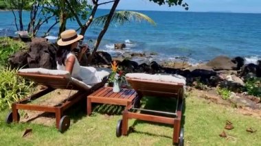 Okyanus kenarında dinlenen Asyalı kadınlar güneşli yataklarla şarap içerken balayı sırasında lüks bir havuzda dinlenen kadınlar Koh Kood Tayland okyanusu manzaralı.