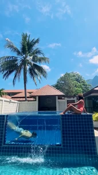 豪華な休暇中にプールヴィラの前でリラックスしたカップル プールでガラス窓で水中で潜水する男性 — ストック動画