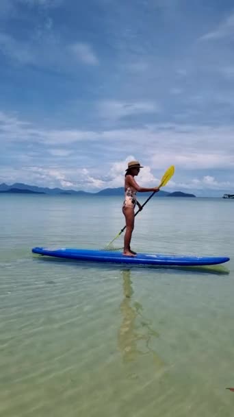 アジア系タイ人女性がタイのコ コッド海でボード上を漕いでいます ターコイズ色の海 — ストック動画