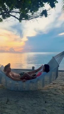 Hua Hin Tayland 'da tropik bir plajda güneşin doğuşunu izleyen bir çift kadın ve erkek. Huahin Tayland sahilindeki hamakta Asyalı kadınlar ve Avrupalı erkekler