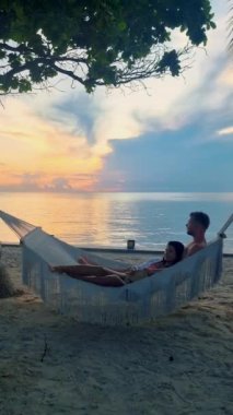 Hua Hin Tayland 'da tropik bir plajda güneşin doğuşunu izleyen bir çift kadın ve erkek. Huahin Tayland sahilindeki hamakta Asyalı kadınlar ve Avrupalı erkekler