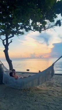 Hua Hin Tayland 'da tropik bir plajda güneşin doğuşunu izleyen bir çift kadın ve erkek. Huahin Tayland sahilindeki hamakta Asyalı kadınlar ve Avrupalı erkekler