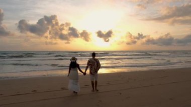 Men and women walking on the beach during sunset in Phuket Thailand. Asian women and European men walking on the beach at sunset 