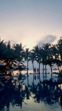 Birkaç erkek ve kadın plaj yataklarında havuzda dinleniyor sandalyeler, tropikal havuz ve okyanusa bakan palmiye ağaçları olan bir havuz.