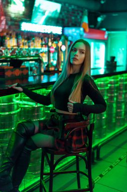 Gece kulübünün açık yeşil barında uzun sarı saçlı çekici bir kadın tezgahta oturuyor. Neon ışıklı kadın model..