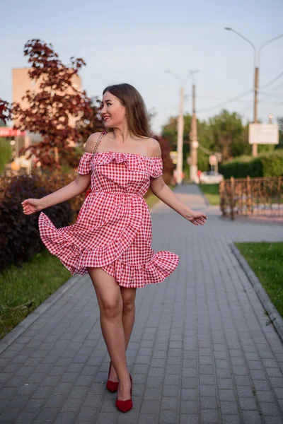 Caddede yürüyen neşeli kız. Kırmızı ekose elbiseli ve kırmızı ayakkabılı genç bir kadın..