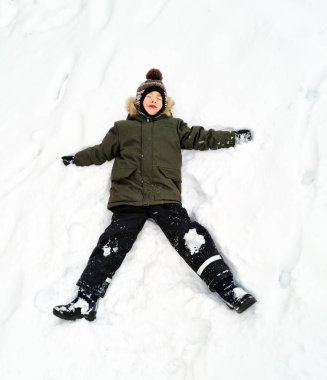 Mutlu ve tatlı çocuk, karda yatan bir kar meleği yapar..