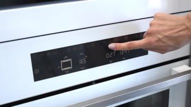 Bir kadının eli yemek pişirmek için beyaz bir fırını açar ve fırının sıcaklığını ve pişirme modunu ayarlar.
