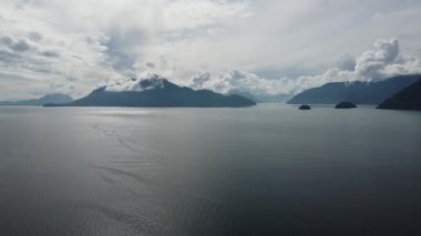 Sular arasında kar beyazı bulutlarla kaplı dağların manzarası