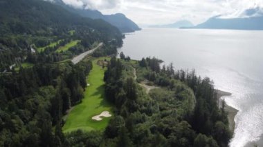 Orman ve su kenarındaki dağların arasındaki bir tarlanın insansız hava aracı görüntüsü.