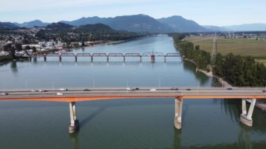 Sıcak bir sonbahar gününde, açık havada, alçak bir kuşun gözünden, kudretli nehri geçen iki köprü.