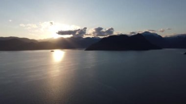 Turuncu güneş, Kanada sularında ve gün batımında etrafındaki dağlarda yansıyor.