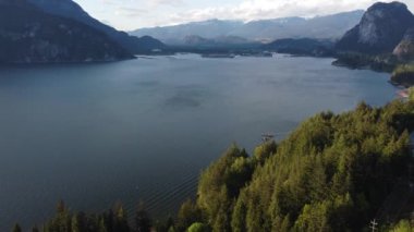 Yeşil ağaçların tepesi, gölün yanındaki dağ bulutlu bir havada.