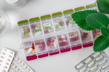 Haplarla dolu iki haftalık ilaç kutusunun üst görüntüsü. Mavi hap kutusu, hafif mermer masanın üstünde. İlaç kutusunu aç ve içinde haplar ya da vitaminler olan kutuları aç. Yaşlı hasta için ilaç kutusu