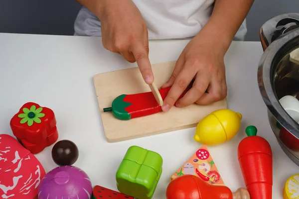 Çocuk ahşap renkli oyuncaklarla oynuyor. Çocuk meyve salatası için ahşap bir biber kesiyor. Çocuklar için eğitici mantık oyuncakları. Çocukların elleri, yakın plan. Çocuk Gelişimi için Montessori Oyunları