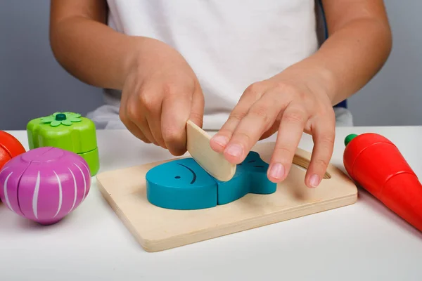Çocuk ahşap renkli oyuncaklarla oynuyor. Çocuk ahşap bir balık kesiyor. Çocuklar için eğitici mantık oyuncakları. Çocukların elleri, yakın plan. Çocuk Gelişimi için Montessori Oyunları